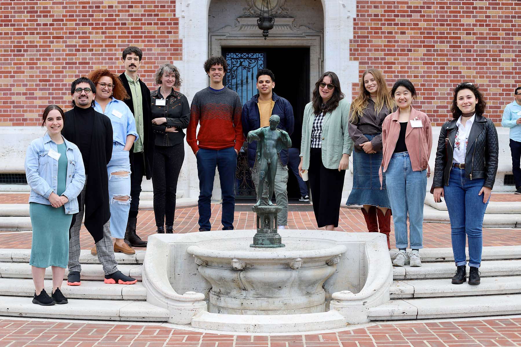 A group of graduate students pose in front of a brick building with a fountain. 