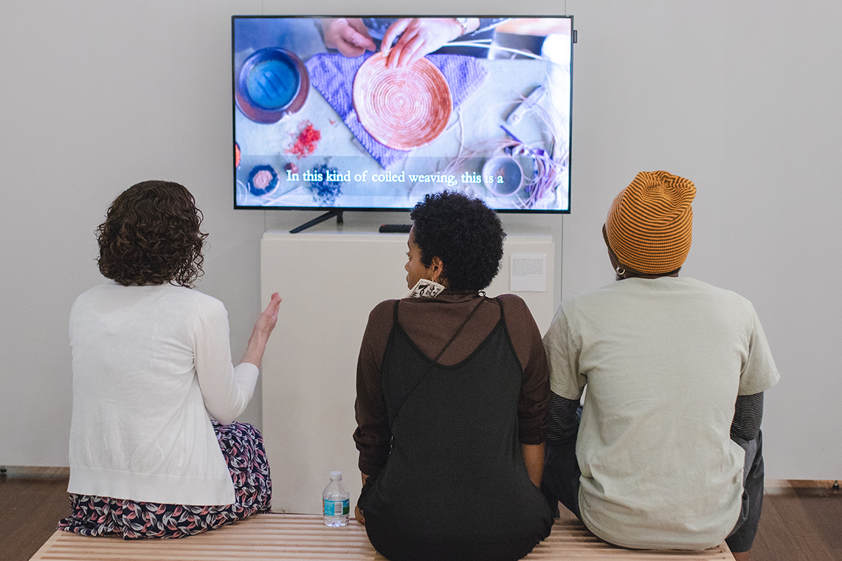 three people sitting on a bench watching a television