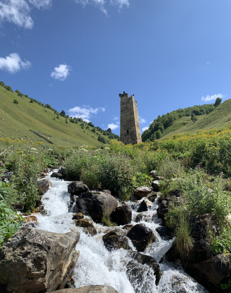 there is a small waterfall in the middle of a field with a tower in the background