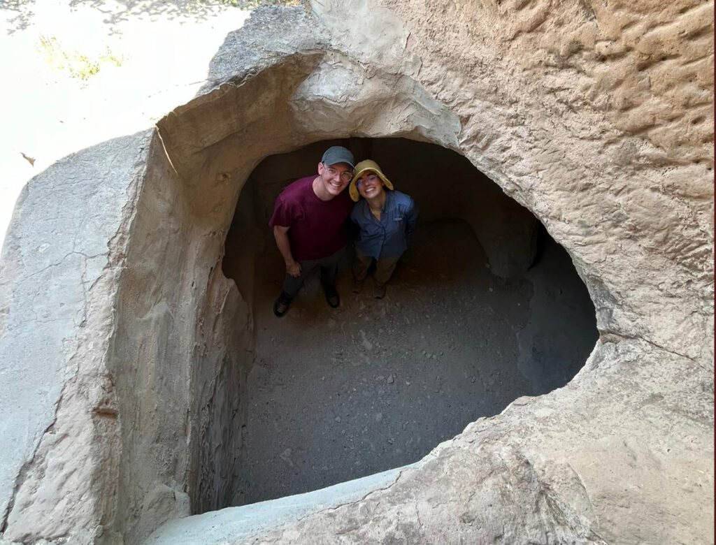 there is a man and a woman standing in a hole in a rock