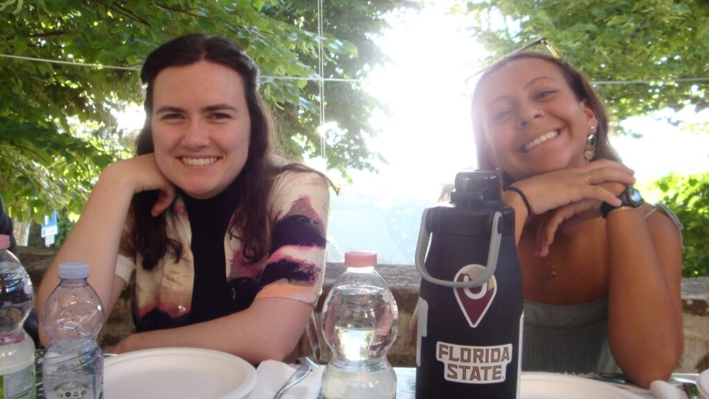 there are two women sitting at a table with a bottle of liquor