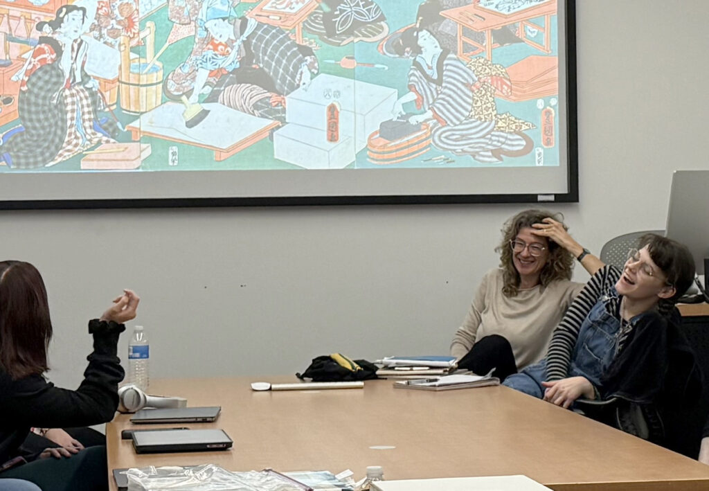 several people sitting around a table with a projector screen in the background