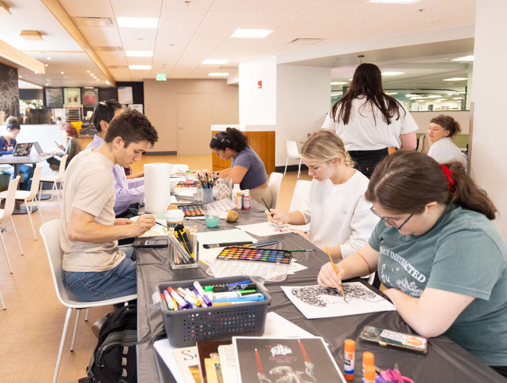 there are many people sitting at a table working on art projects
