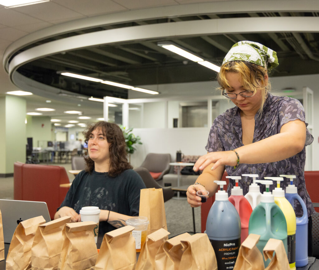 there are two women sitting at a table with bags of cleaning products