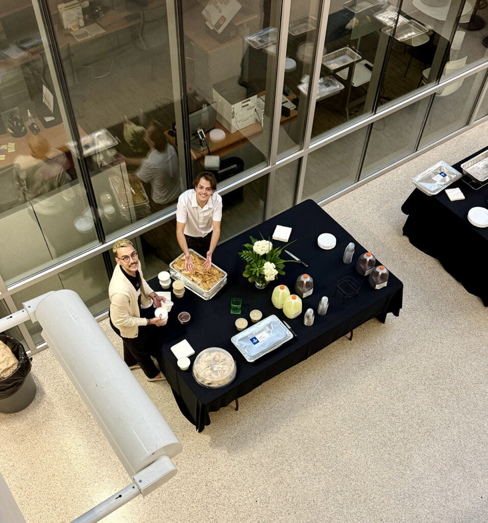 there are two people that are standing around a table with food on it