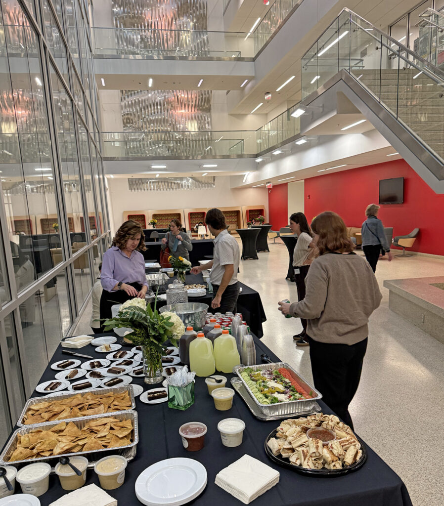 there are many people standing around a long table with food on it