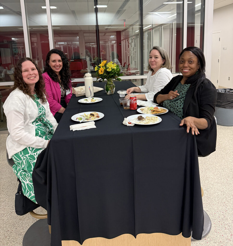 there are four women sitting at a table with plates of food
