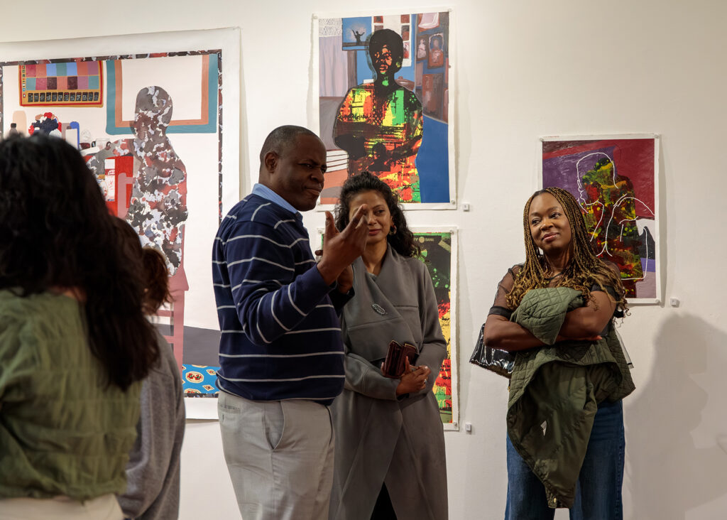 several people standing in front of a group of paintings on a wall