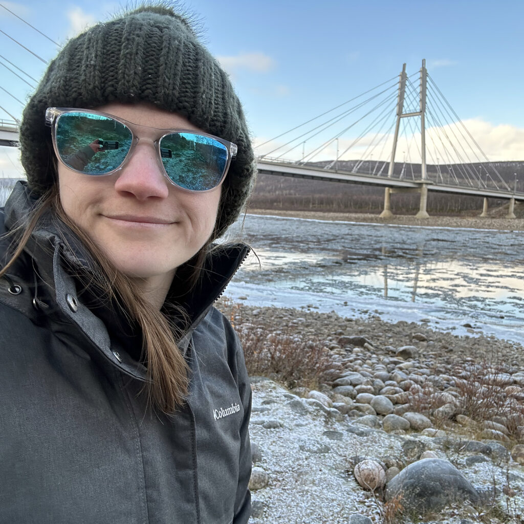 there is a woman wearing sunglasses and a hat standing in front of a bridge