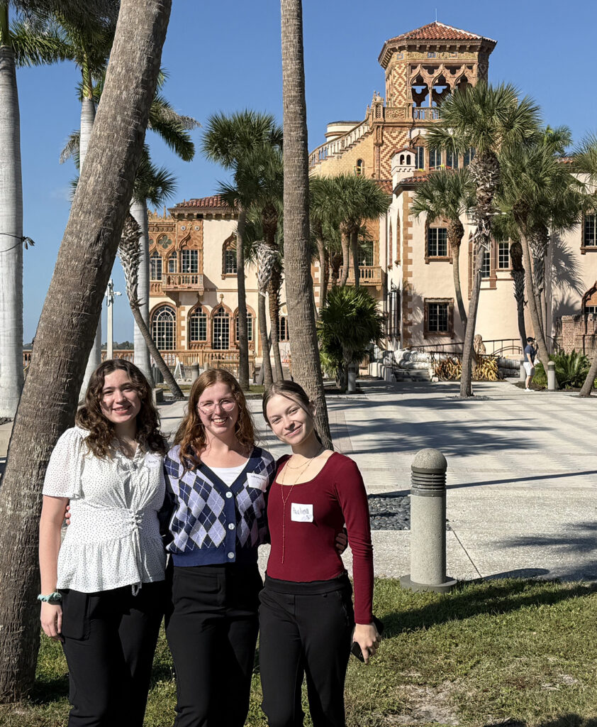 three women standing next to each other in front of a building