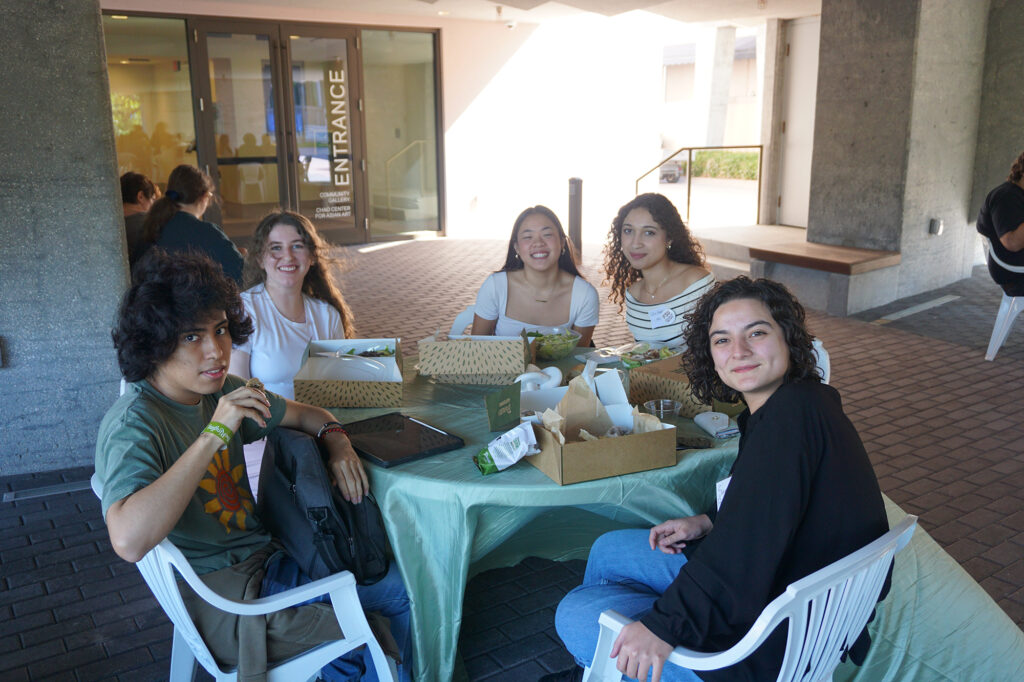 several people sitting at a table with boxes of food on it