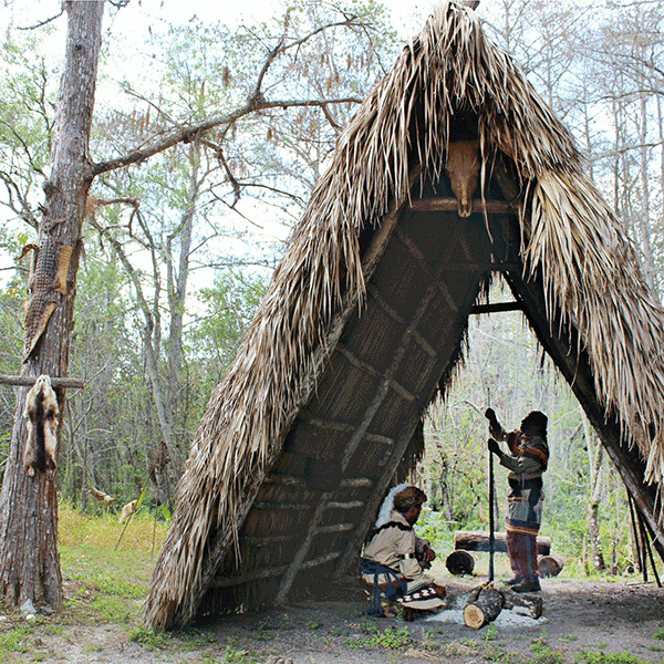 there are people that are standing outside of a hut in the woods