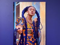 A photograph of a woman in an African print dress displayed on a blue wall.